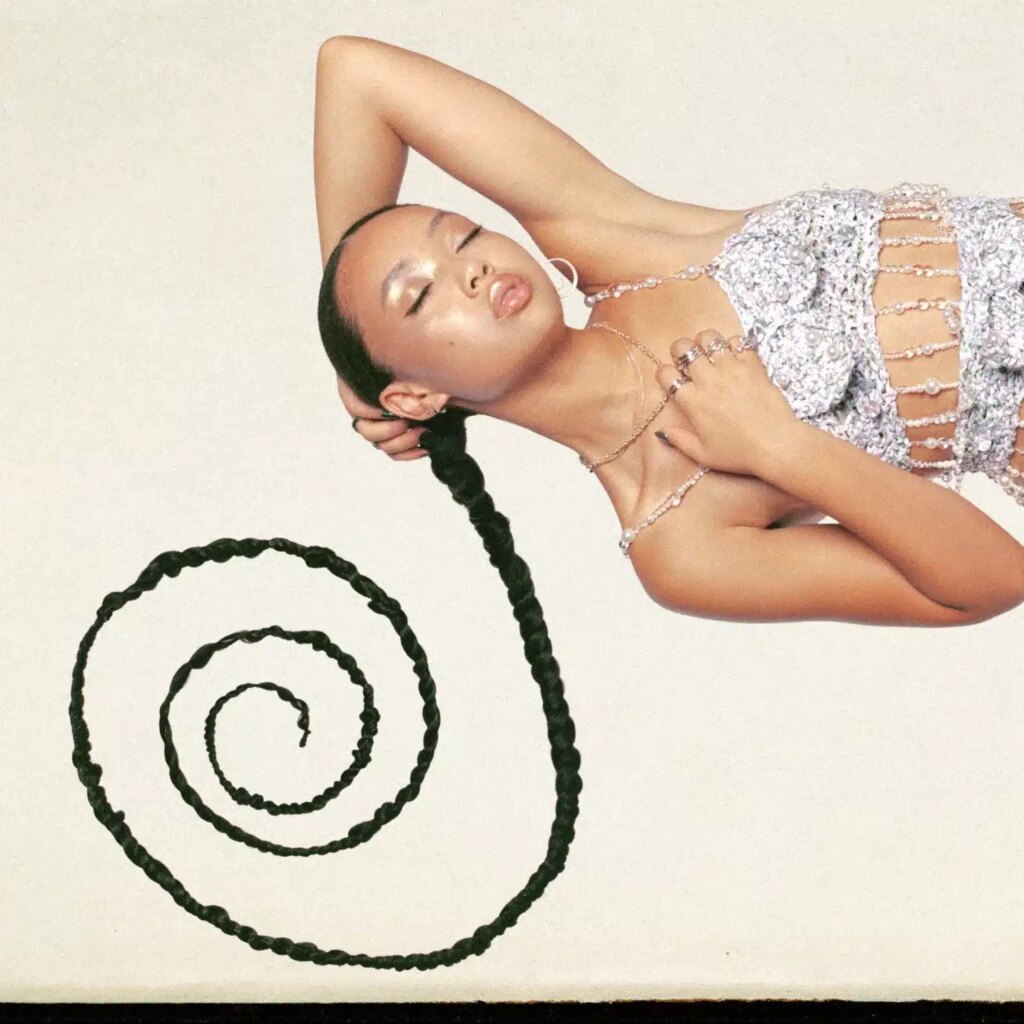 Griff posing with a long braided ponytail spiraling outward, wearing a sparkling, beaded top, eyes closed in a serene, stylish expression.