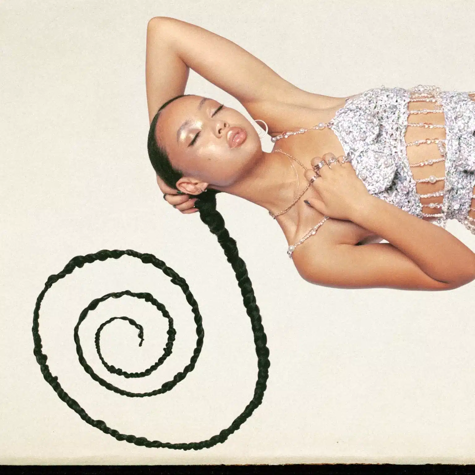 Griff posing with a long braided ponytail spiraling outward, wearing a sparkling, beaded top, eyes closed in a serene, stylish expression.