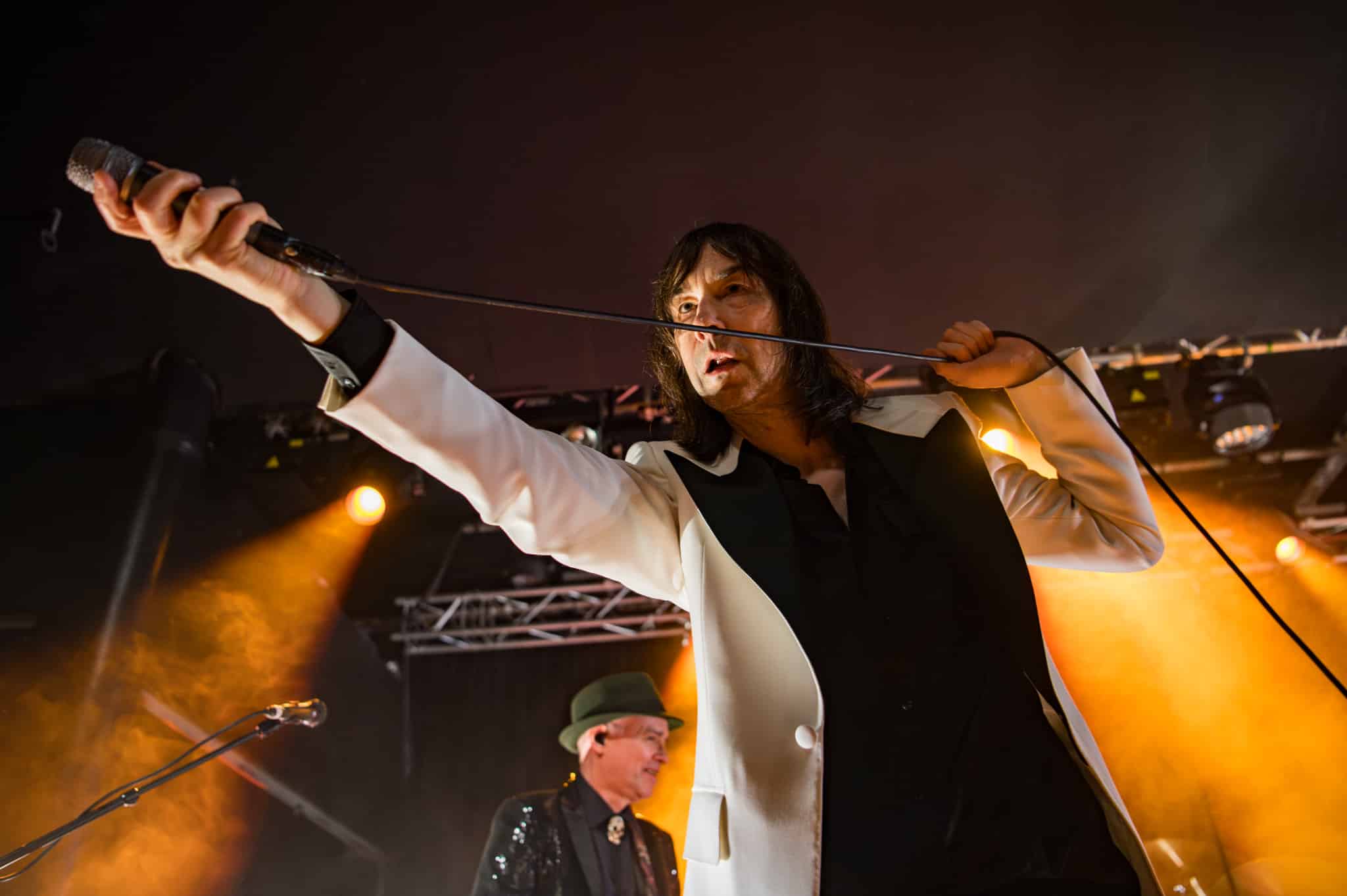 Primal Scream's Bobby Gillespie reaching out to the crowd at Rock City under yellow lighting.