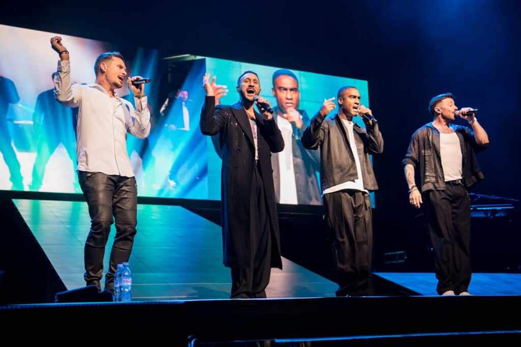 Blue performing at First Direct Arena, Leeds, surrounded by bright lights and cheering fans