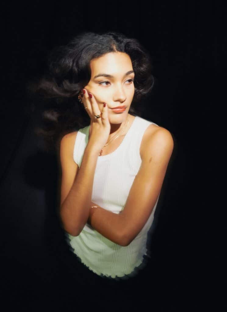 Olivia Dean looking pensive whilst wearing a white vest top