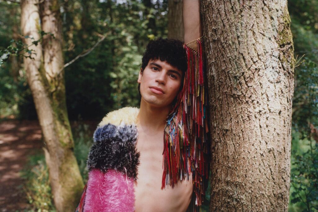 Jacob alon leans against a tree whilst wearing a sparkly jacket