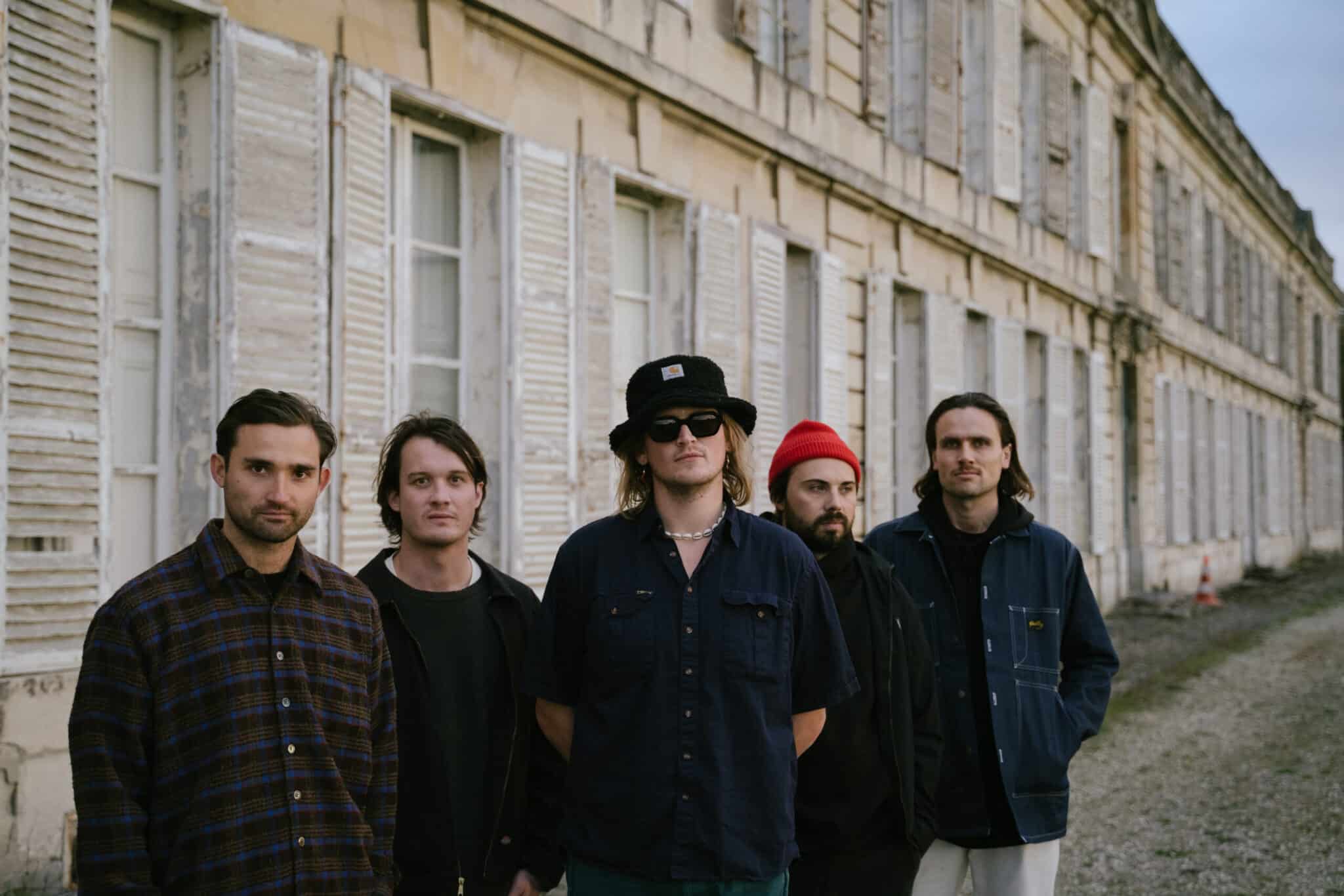The 5 members of the band NO CIGAR stand outside a building wearing dark clothing